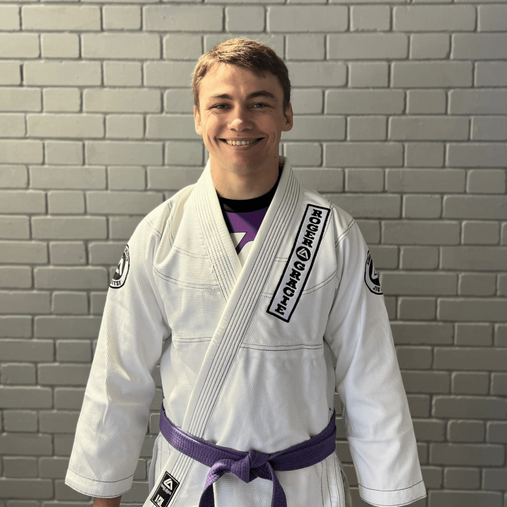 Purple belt male assistant coach smiling at the camera in his Gi.